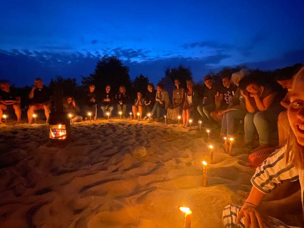 Een groep zit samen rondom een kampvuur op het strand